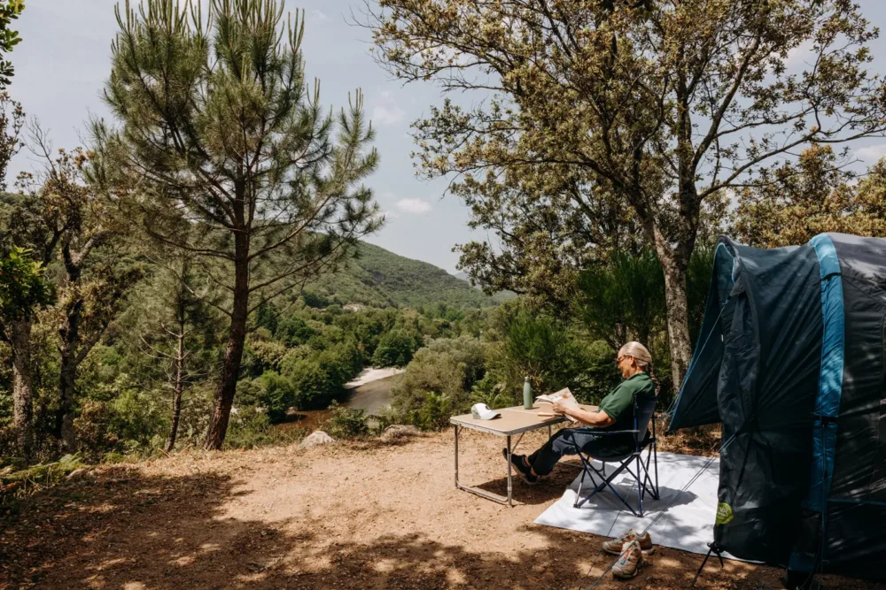 Une campeuse contemple le paysage, assise sur sa chaise.